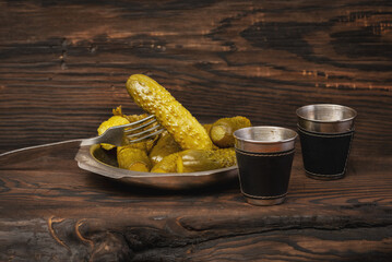 Close-up of a plate of pickles on a wooden table with two metal cups