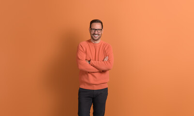 Portrait of determined young businessman with arms crossed posing confidently on orange background