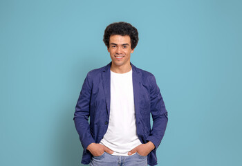 Portrait of smiling businessman with afro hairstyle and hand in pockets posing on blue background