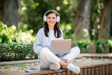 Young woman with headphones using a laptop in park