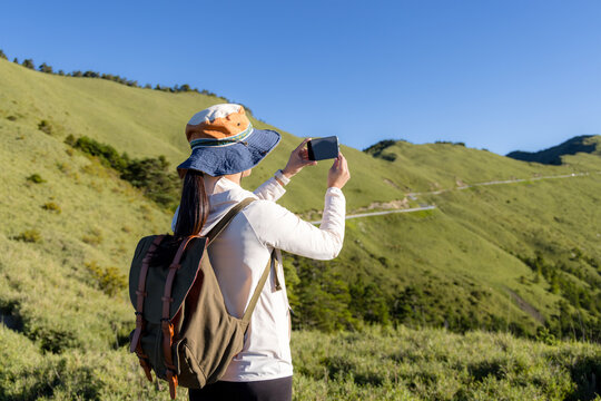 Hiking woman enjoy the beautiful view and use of mobile phone to take photo at mountain peak