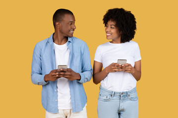 Couple engaged in conversation with phones on yellow - 779896953