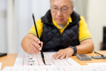 Asian old man practice Chinese characters with calligraphy at home