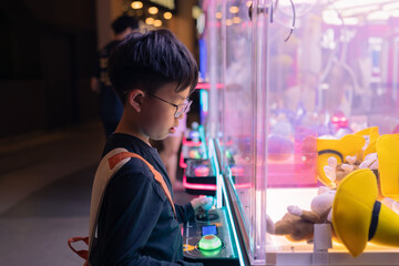 Asian boy at one of the mall stores, playing Claw Game.