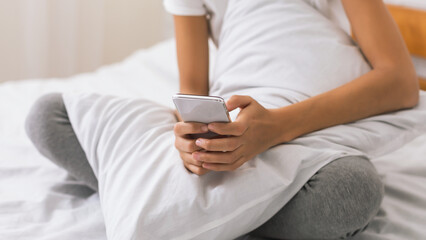 Young woman using smartphone and resting in bed