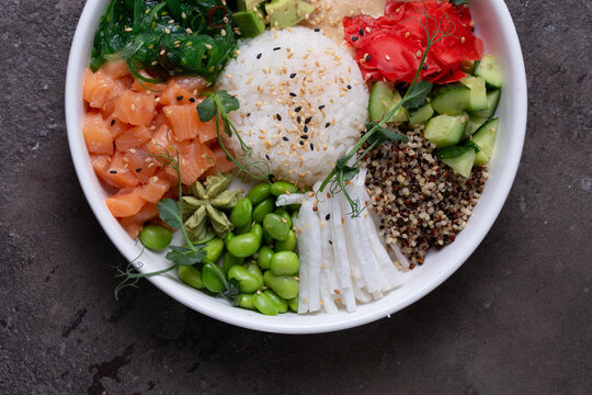 Top view of a bye bowl with salmon, avocado, cucumber, sprouts and rice on a white plate