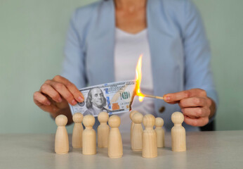 A businesswoman burns 100 banknotes and figurines of society people - obrazy, fototapety, plakaty
