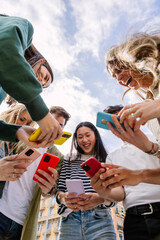 Vertical photo of young adult friends using mobile phone together outside. Gen Z people generation...