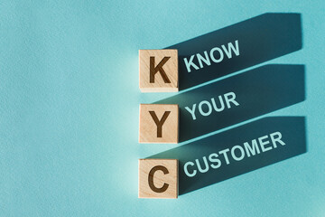 Wooden blocks with letters spelling out KYC, acronym for Know Your Customer, cast shadows on a blue...