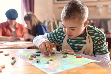 Close up portrait of young boy with Down syndrome drawing picture and smiling during art therapy class