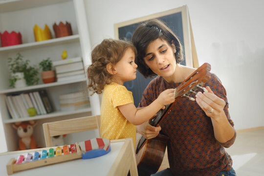 Mother and child playing with music instruments at home. Mother learning kid to play guitar. 