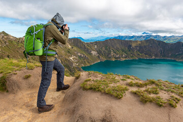 Male photographer in trekking outfit taking photographs of the Quilotoa Lagoon along the Quilotoa...