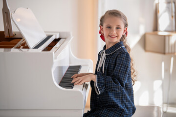 A little girl plays a big white piano in a bright sunny room