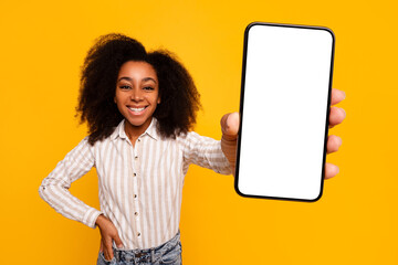 Smiling woman displaying smartphone screen on yellow background