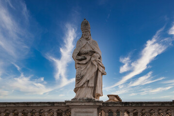 Stone statue of religious figure in Vatican City, adorned in ecclesiastical garments, holding a...