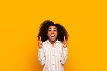 Excited young woman pointing up on yellow