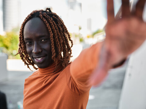 South Sudanese man wearing orange turtleneck reaching towards the camera