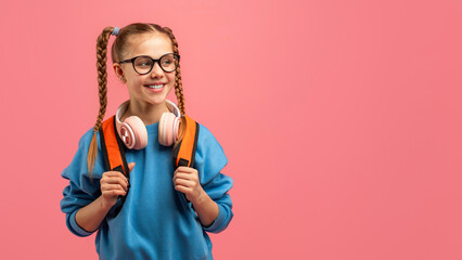 Joyful student with headphones on pink backdrop