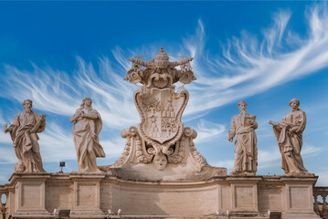 Statues with ornate coat of arms under a dramatic sky in Vatican City. Classical sculptures and symbolic imagery provide historical and religious significance.