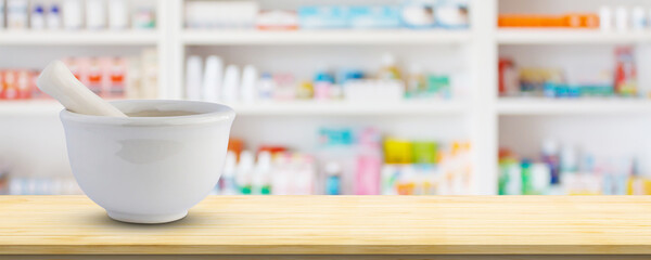 Mortar and pestle on pharmacy counter top with blur medicine shelves in drugstore background - obrazy, fototapety, plakaty