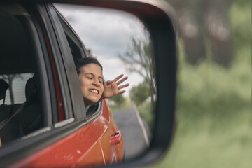 Teenage girl sticking her face with her hand out of the car window to catch the wind from the...