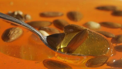 Healthy organic honey. Sweet fresh golden honey on the yellow background, spoon scooping almonds walnuts and cashew nuts covered in the thick syrup, close up shot.