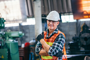 Portrait of male foreman factory wearing hardhat in arms crossed and showing thumb up looking at...