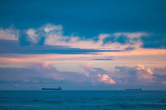 Cargo ships lined up at sea on their way to Newcastle Harbour under a vibrant sunset sky