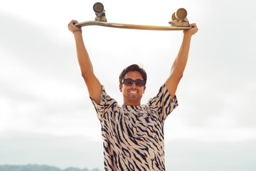 portrait handsome latin guy holding a skateboard over his head outdoors on the beach	