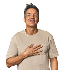 Middle-aged Latino man laughs out loudly keeping hand on chest.