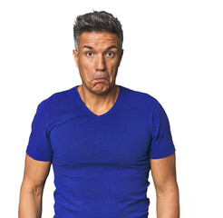 Middle-aged Latino man shrugs shoulders and open eyes confused.