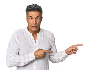 Middle-aged Latino man shocked pointing with index fingers to a copy space.