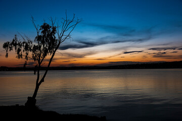 Fototapeta na wymiar Silhueta de árvore cores do céu do pôr do sol, refletindo na textura da agua da lagoa