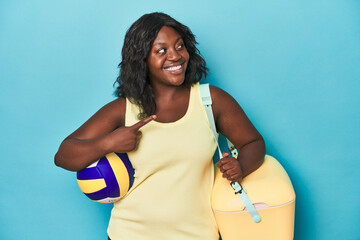 Young curvy woman with cooler and ball smiling and pointing aside, showing something at blank space.