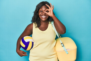 Young curvy woman with cooler and ball excited keeping ok gesture on eye.