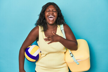 Young curvy woman with cooler and ball laughs out loudly keeping hand on chest.