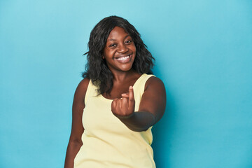Young african american curvy woman pointing with finger at you as if inviting come closer.