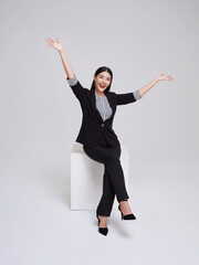 Attractive beautiful Asian woman sitting on white chair and hands up raised arms from happiness, Excited businesswoman winner success concept