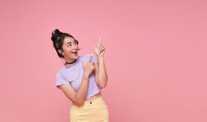 Smiling young asian teen girl looking and pointing finger shows place for your advertising text Isolated on pink background.