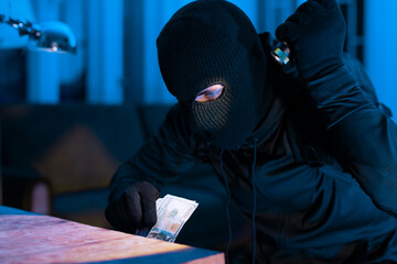 Burglar counting stolen money in dim light © Prostock-studio