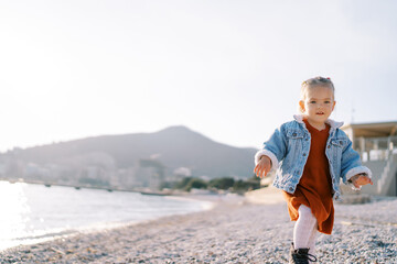 Little girl walks along a pebbly beach near the sparkling sea