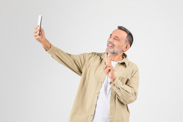 Mature man taking selfie with smartphone on white background