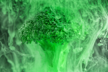 Fresh broccoli with a cloud of green color paint in water. Artistic nutrition concept. Science of...