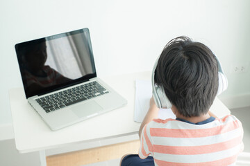 Back side of Asian school boy learning online using a laptop computer and headphones
