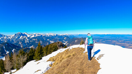 Woman on panoramic hiking trail on way to snow covered mountain peak Ferlacher Horn in Carinthia,...