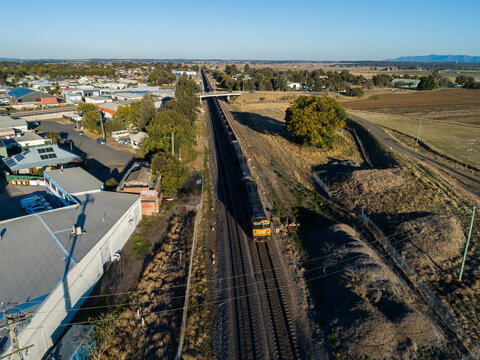 Train engine pulling empty coal train carriages along edge of country town
