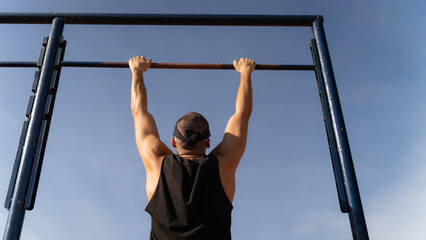 Man performing suspension on pull-up bar. In the background the blue sky for copy space. Concept of sport and physical health