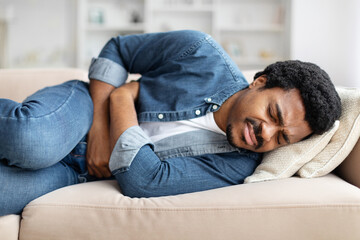 Black Man Experiencing Stomach Pain While Lying on Couch At Home