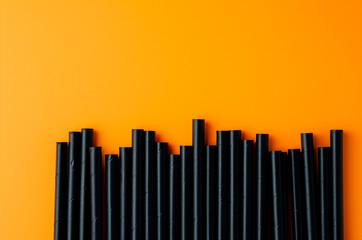 Black straws on an orange background, cocktail straws for Halloween, ecology, design