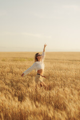 A joyful young woman with arms raised in a vast, golden wheat field under the open sky, conveying a sense of freedom, summer, and happiness.